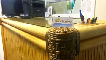 Una mesa de recepción con un cartel de Palm Villa Suites & Convenience Store, una computadora y un portalápices con bolígrafos.