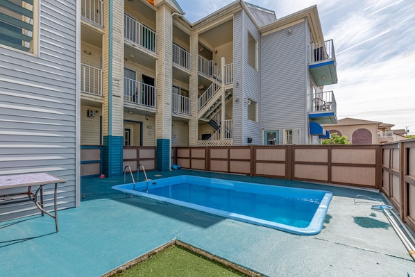 A multi-story building with a swimming pool, balconies, and a fenced patio area.