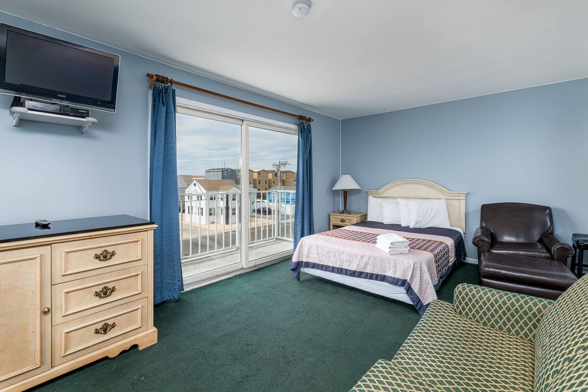 Habitación de hotel con cama, televisión, cómoda, silla y vistas a edificios.