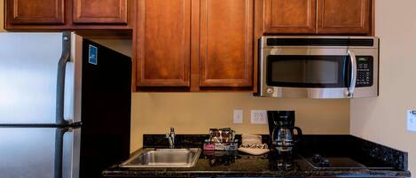A kitchen with wooden cabinets, a stainless steel refrigerator, a microwave, a dishwasher, and a coffee maker.