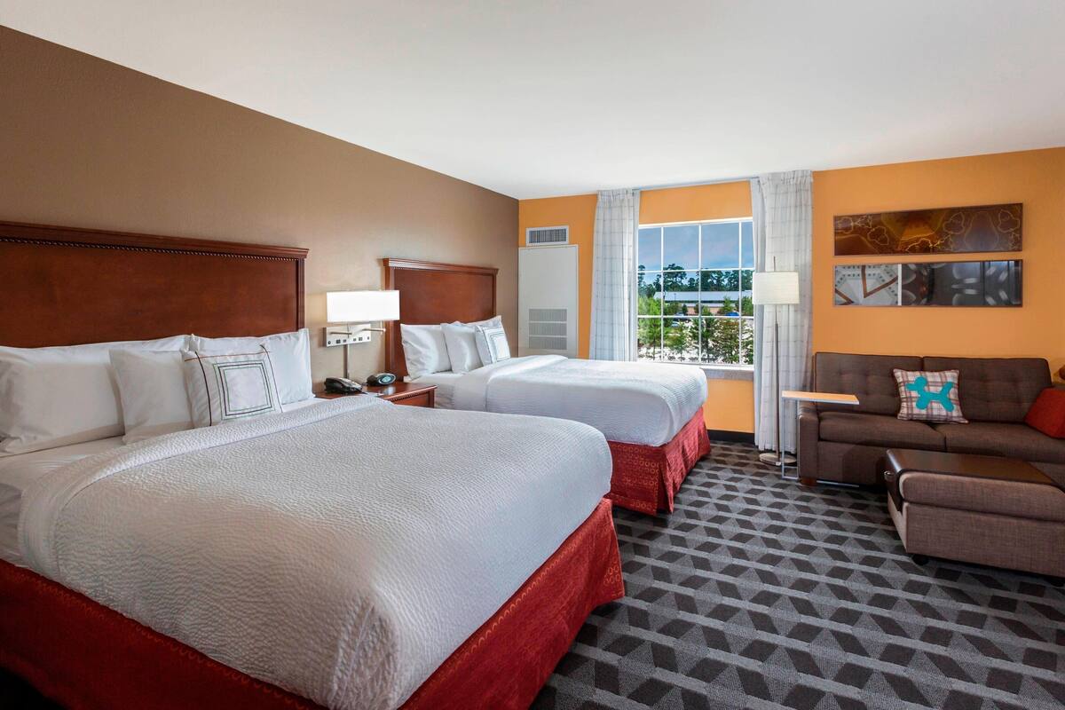 A hotel room with two beds, a sofa, a TV, and a window with a view.