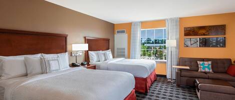 A hotel room with two beds, a sofa, a TV, and a window with a view.