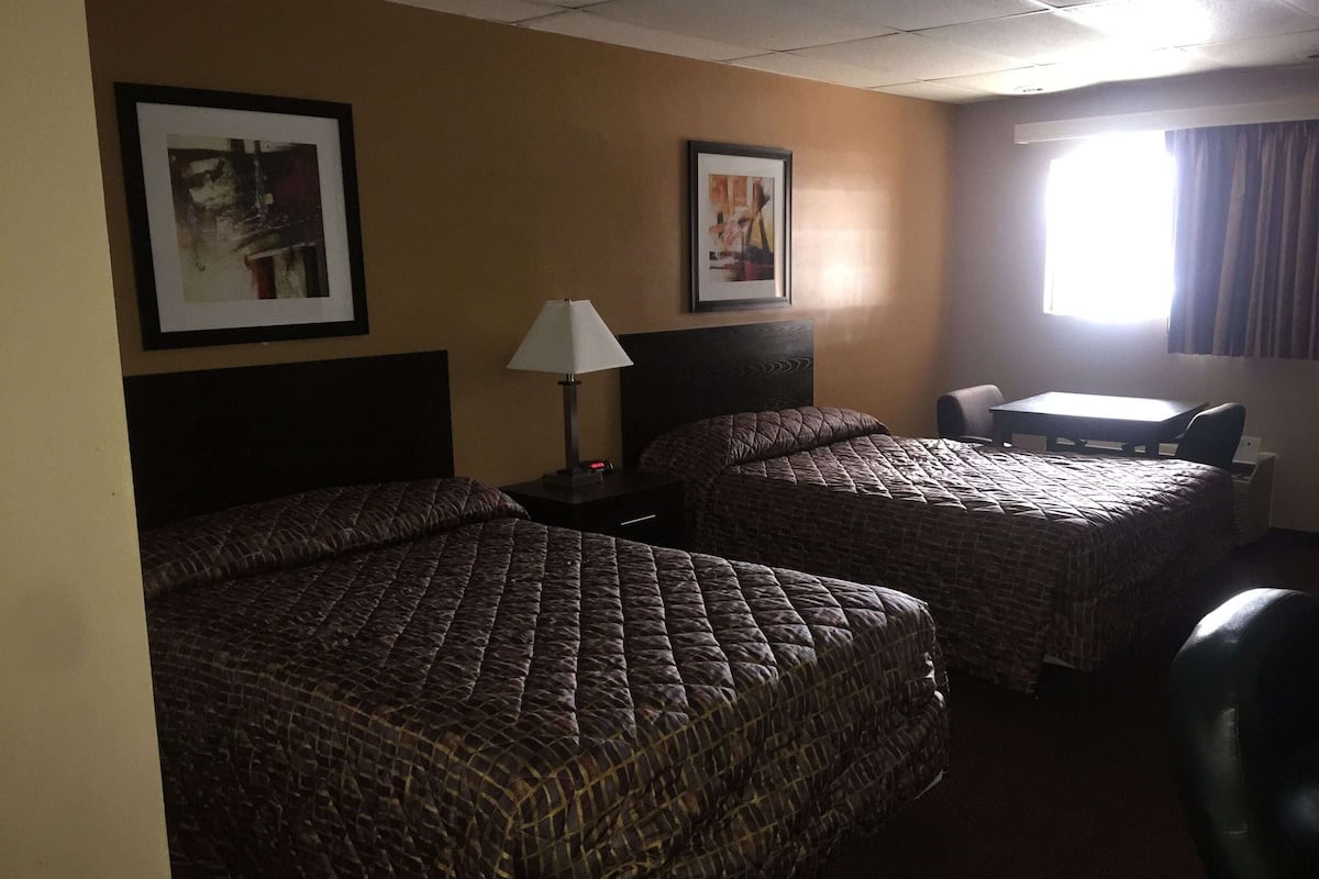 A hotel room with two beds, a desk, a chair, a lamp, and two framed pictures on the wall.