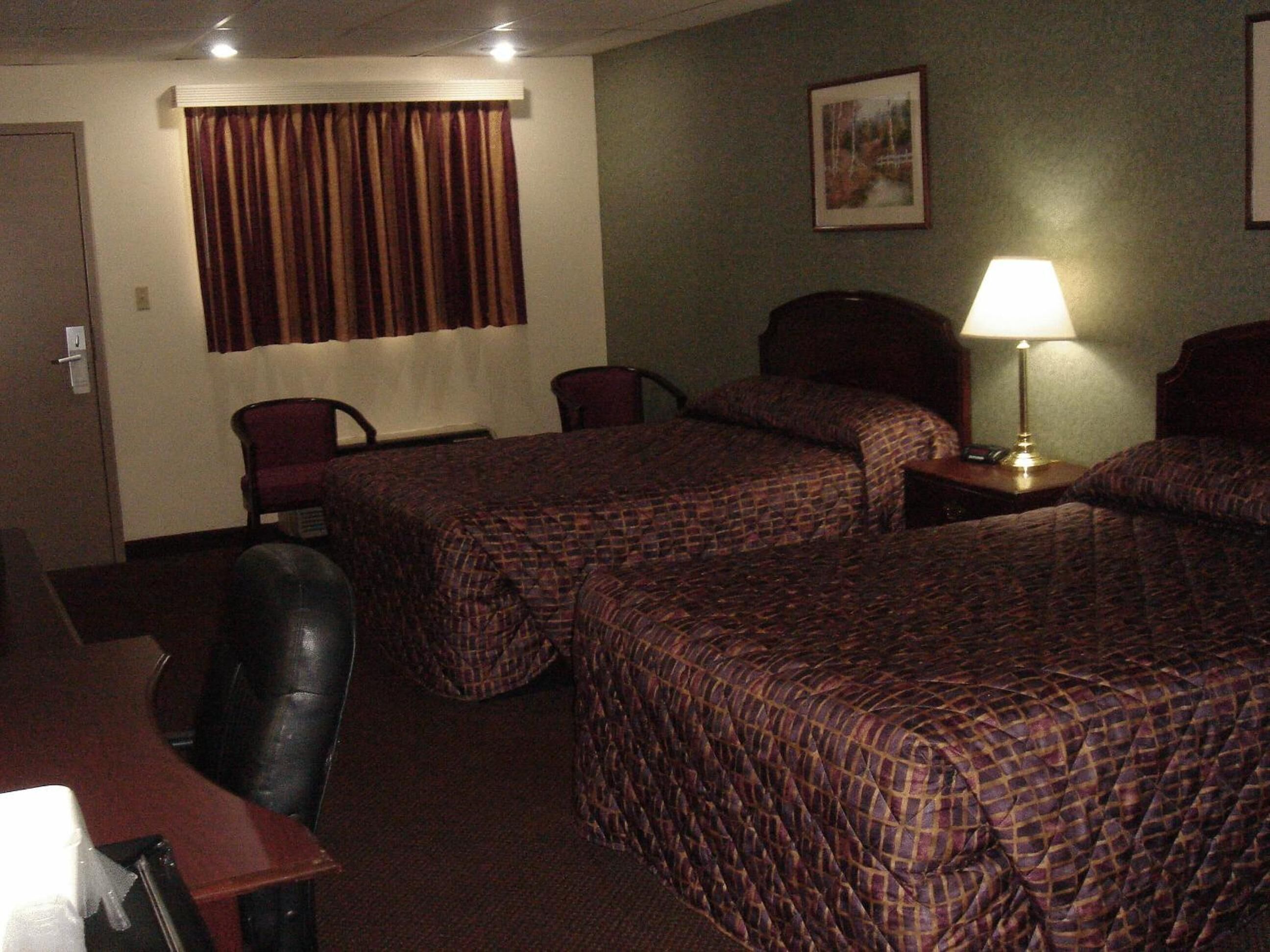 A hotel room with two beds, a desk, a chair, a lamp, and a picture on the wall.