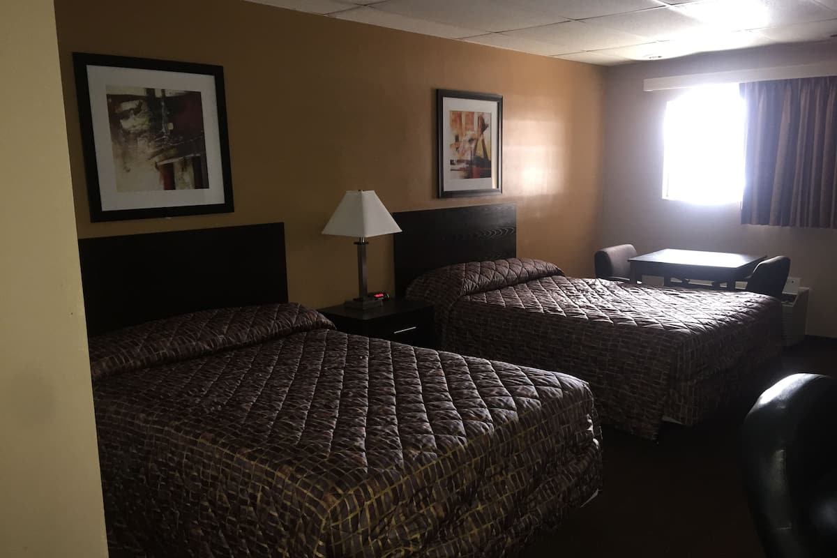 A hotel room with two beds, a desk, a chair, and two framed pictures on the wall.