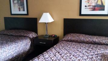 A hotel room with two beds, a nightstand with a lamp, and two framed artworks on the walls.