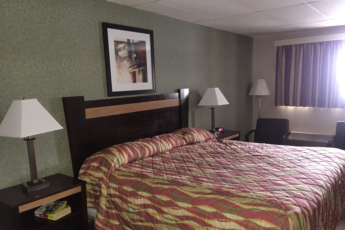 A hotel room with a large bed, two bedside lamps, a framed picture on the wall, and a desk with a chair.