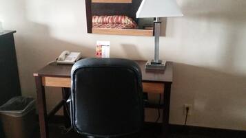 Habitación de hotel con escritorio, una silla de oficina negra, lámpara, teléfono y cubo de basura.