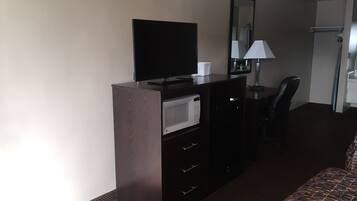 A hotel room with a flat-screen TV, a microwave, a desk with a chair, and a bed.