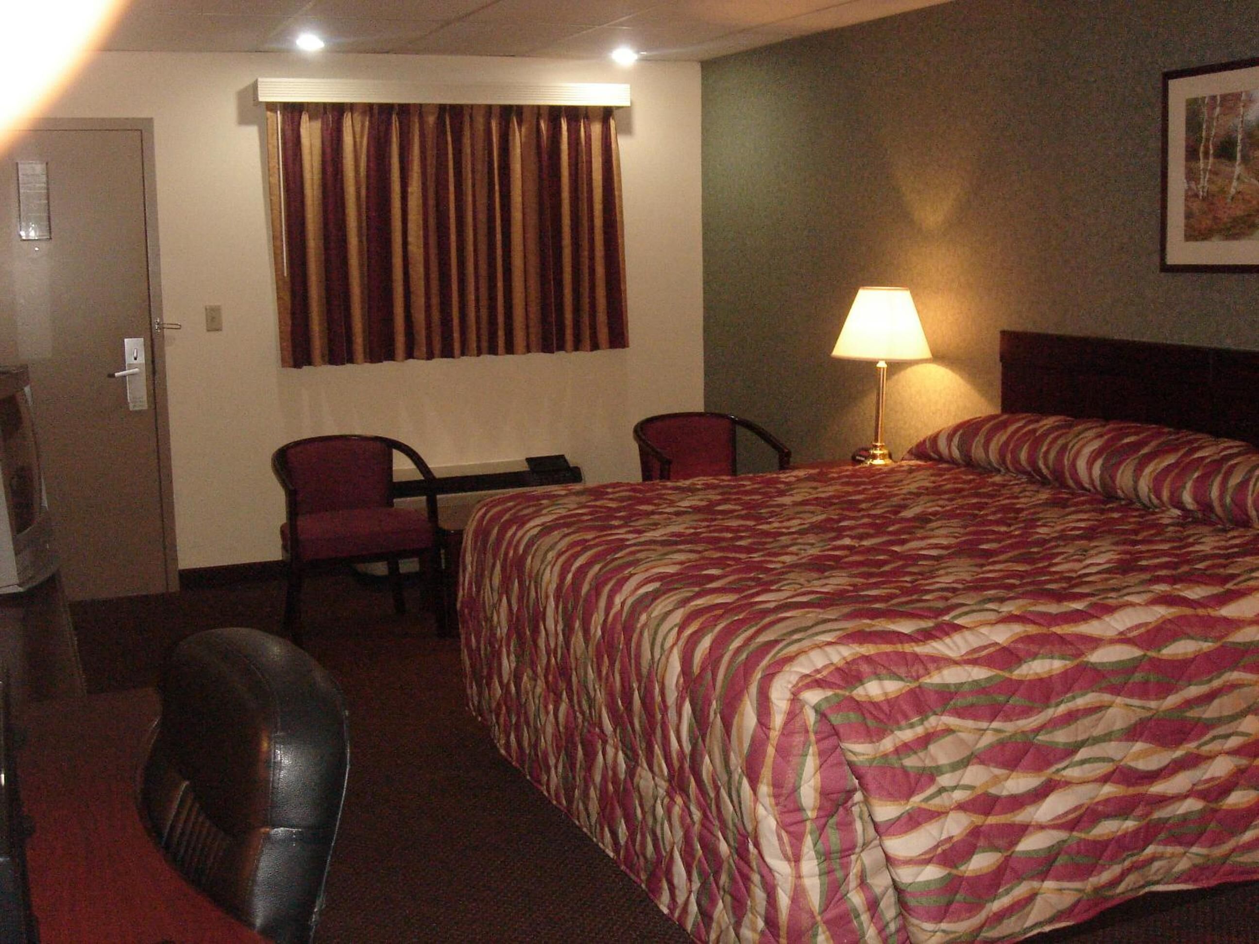 A hotel room with a large bed, a desk, two chairs, a lamp, and a door.