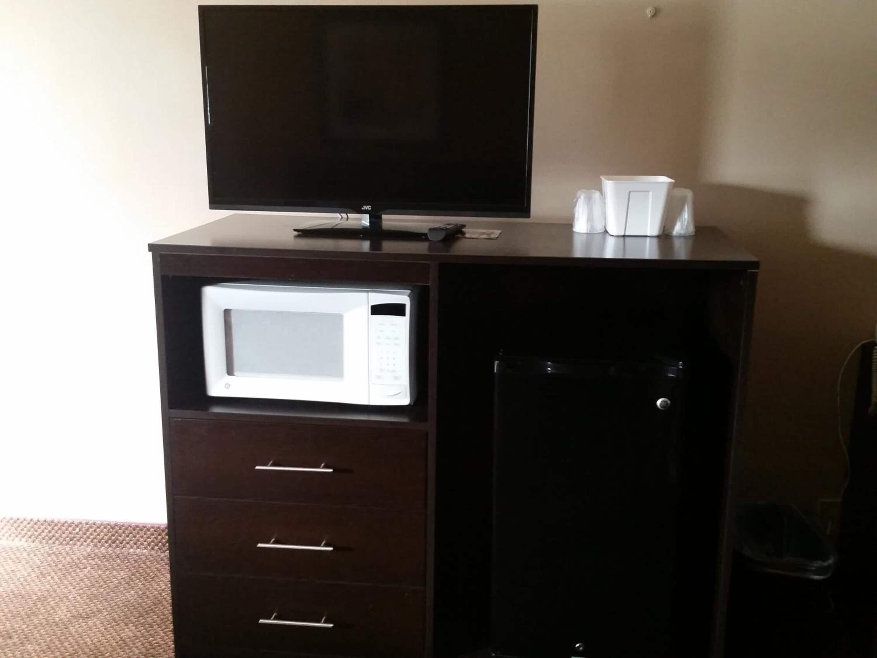 Un armario de madera oscura con un microondas blanco, un refrigerador pequeño y un televisor encima.