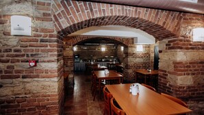 Un restaurante de paredes de ladrillo con mesas y sillas de madera, una cocina al fondo y un techo abovedado.