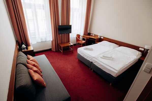 Habitación de hotel con cama, escritorio, silla, televisor y ventana con cortinas.
