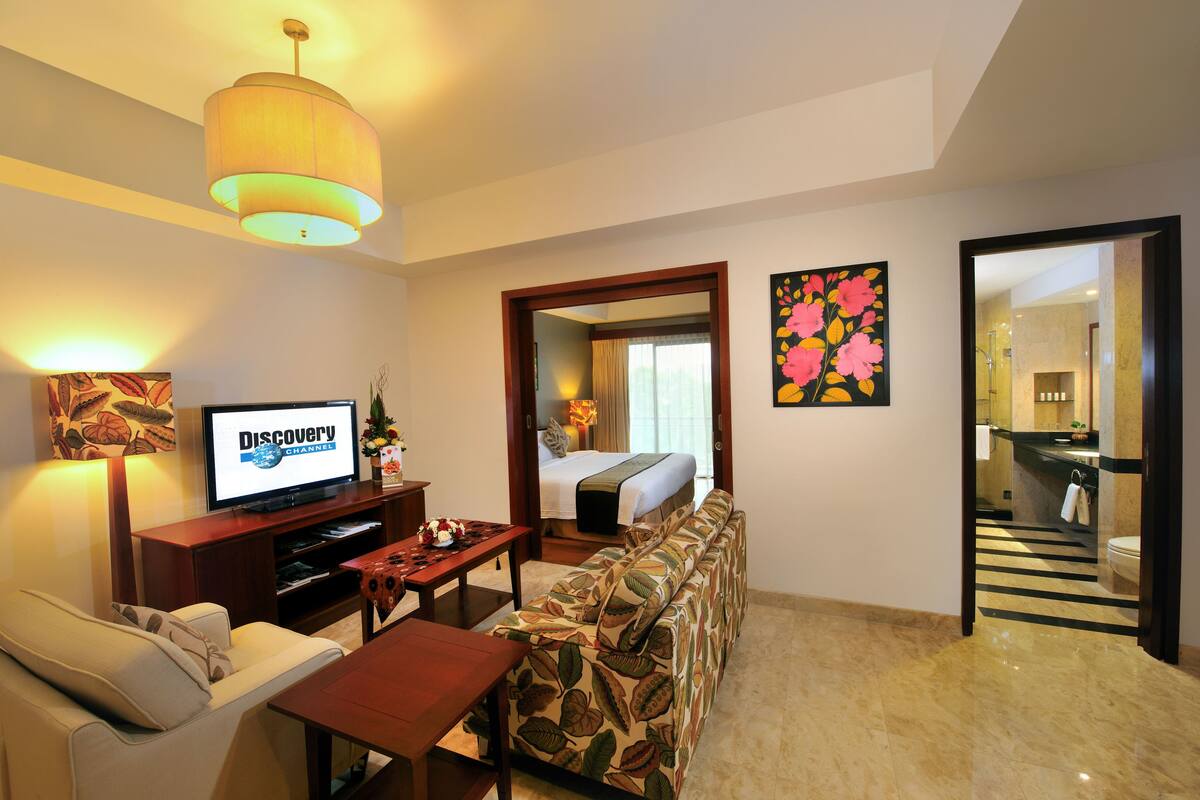A hotel room with a television, sofa, dining table, and a mirror reflecting the room.