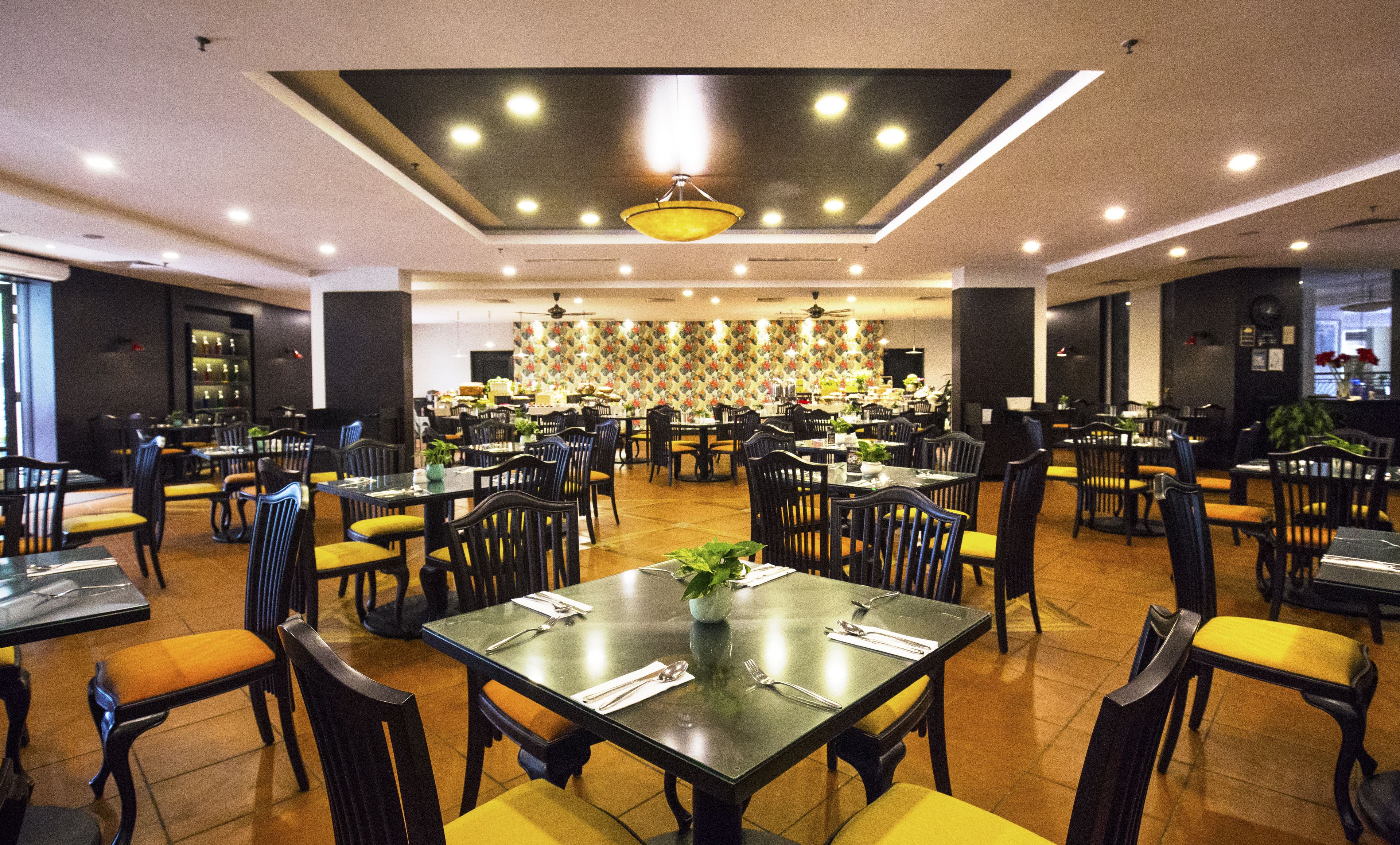A spacious restaurant with multiple dining tables and chairs, a central decorative wall, and a ceiling light fixture.