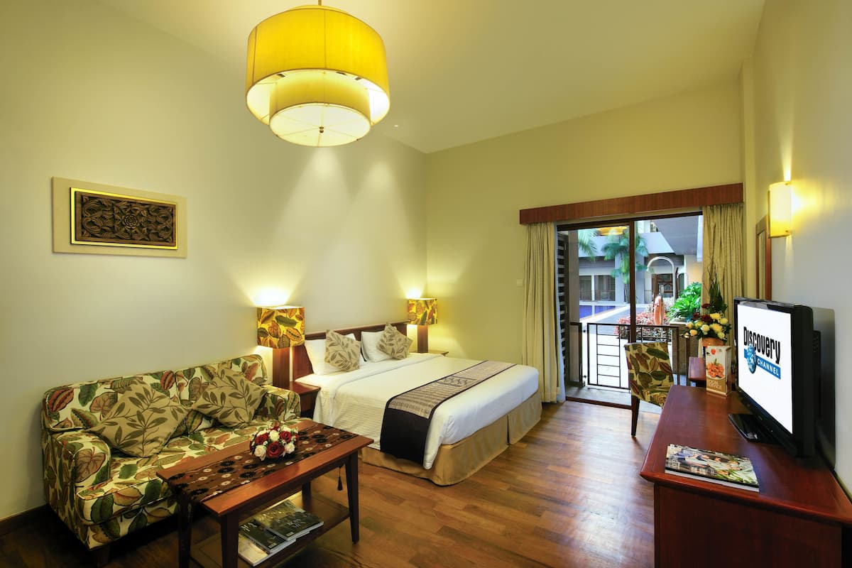 A hotel room with a bed, a sofa, a coffee table, a TV, and a balcony with a view.