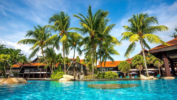 A swimming pool with clear blue water, surrounded by palm trees and a building with a red roof. - Pulai Springs Resort (Johor Bahru)