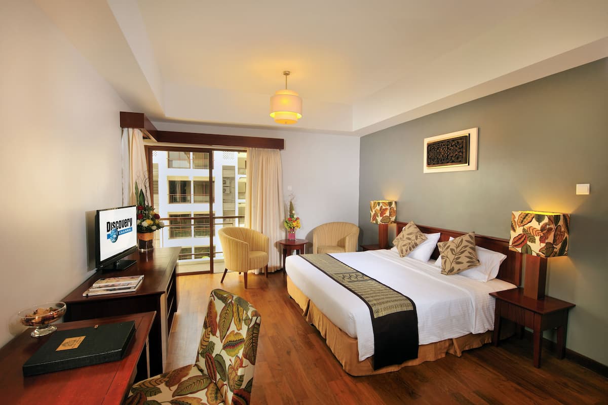A hotel room with a bed, two chairs, a desk with a computer, a lamp, and a window with curtains.