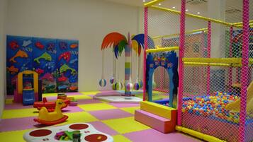 Zona de juegos infantiles con piscina de pelotas, estructuras de juego coloridas y suelo acolchado.