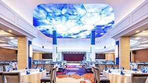 Una sala de conferencias con un gran panel hexagonal en el techo, varias mesas con sillas y un escenario al frente.