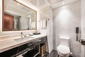 A modern bathroom with a large mirror, a white sink, a black vanity, a toilet, and a marble wall.