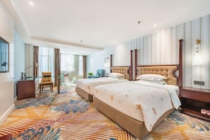 A hotel room with two beds, a sitting area with a chair, a desk, and a large window.