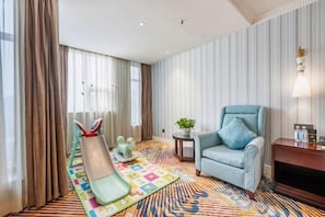A hotel room with a striped wall, a blue armchair, a small table with a plant, and a colorful rug.