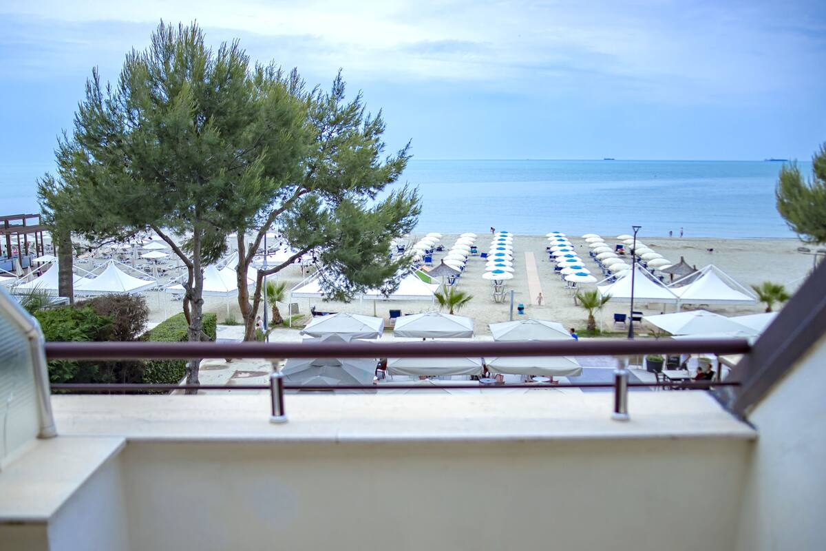 Vista al mar desde un balcón, con hileras de sombrillas y sillas de playa.