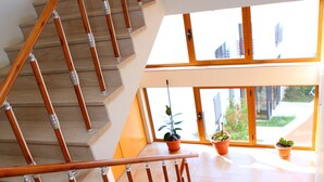 A modern staircase with wooden handrails and beige steps, leading to a balcony with potted plants and a view of buildings. - Hotel Oaz (Golem)