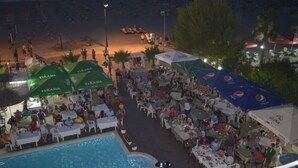 An outdoor pool area with dining tables and umbrellas, surrounded by beach chairs and a swimming pool. - Hotel Oaz (Golem)