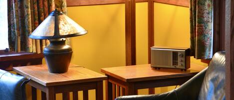 Una habitación con una mesa de madera, una lámpara, una radio y un sillón de cuero.