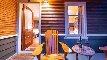 A wooden exterior with a door leading to a room, a wooden chair, and a table with two glasses of red wine.