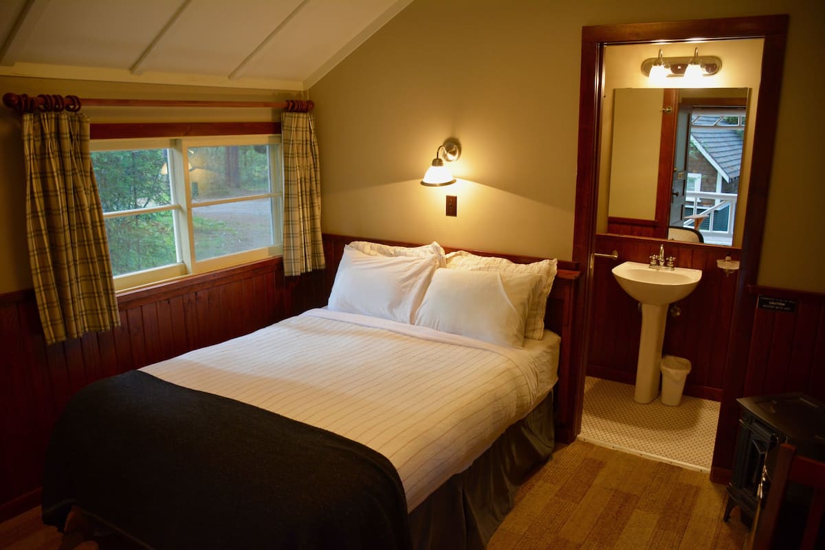 Een slaapkamer met een groot bed, een raam met gordijnen, een bedlampje, een wastafel en een spiegel.