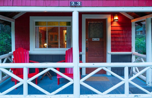 A red building with a white porch, a welcome sign, and two red chairs.