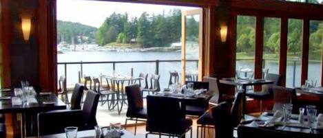 Ein Restaurant mit gedeckten Tischen, große Fenster mit Blick auf einen See und einen Wald.