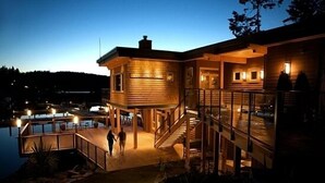 A wooden cabin with a glass balcony, a staircase, and a pool area at dusk. - Painted Boat Resort (Madeira Park)