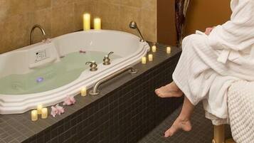 Relax in a serene bathroom with a bathtub and control panel, surrounded by candles and a comfortable reading chair.