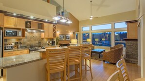 A modern kitchen with granite countertops, wooden bar stools, and a dining area with a stone fireplace. - Painted Boat Resort (Madeira Park)