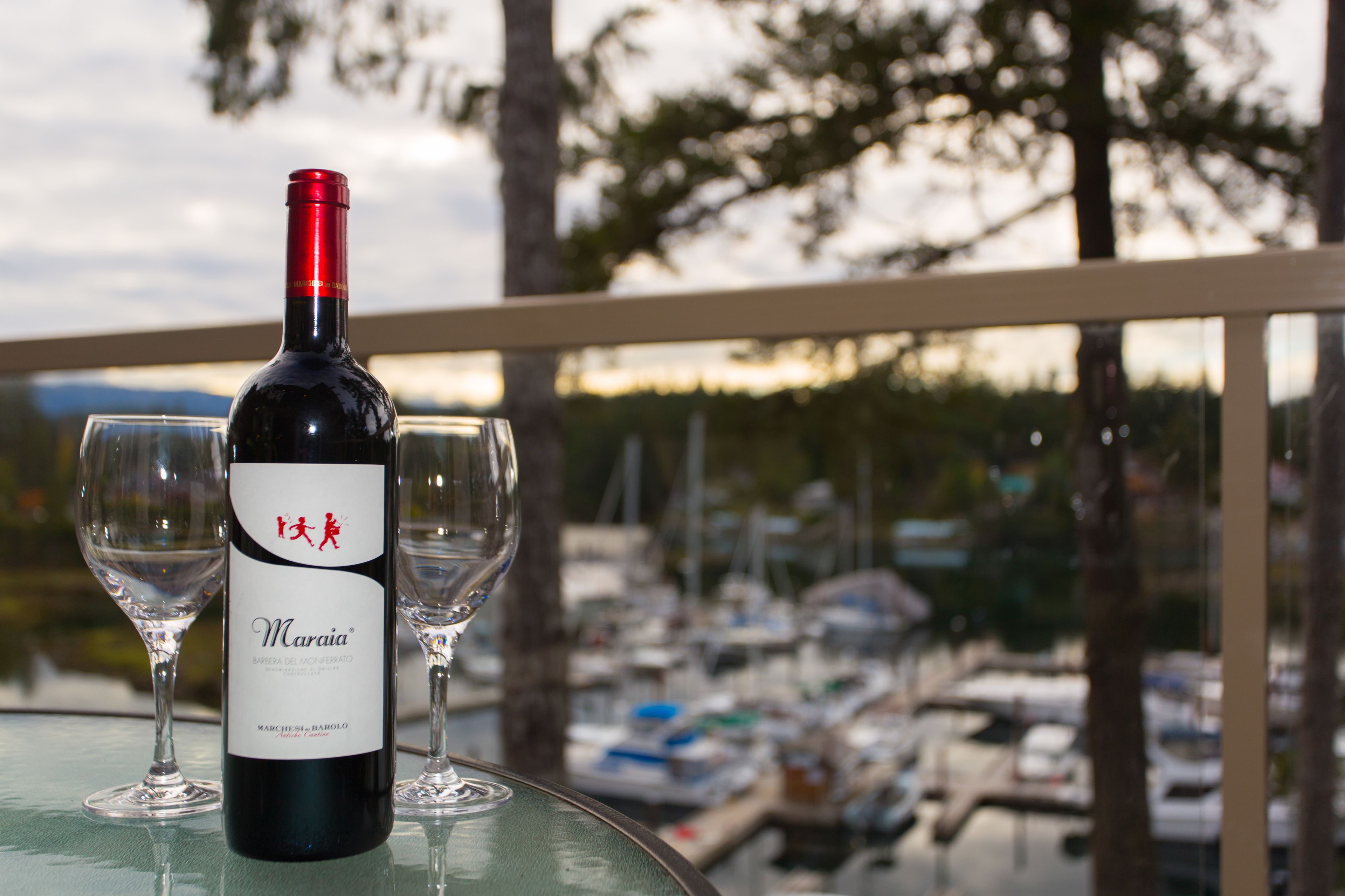 A bottle of wine and two glasses on a table with a view of a marina.