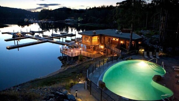 A lakeside property with a swimming pool, dock, and a house with outdoor lighting. - Painted Boat Resort (Madeira Park)