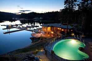 A lakeside property with a swimming pool, dock, and a house with outdoor lighting. - Painted Boat Resort (Madeira Park)