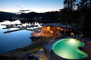 Propiedad frente al lago con piscina, muelle y casa con iluminación exterior.