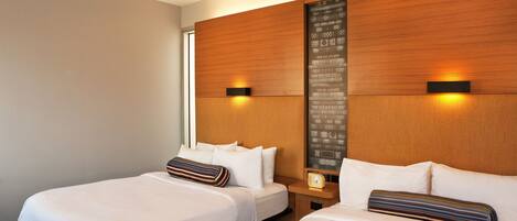 A hotel room with two beds, a wooden headboard, a nightstand with a clock, and a wall-mounted light fixture.