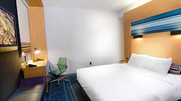 Une chambre d’hôtel avec un lit, un bureau et une chaise, une lampe et un tableau au mur.