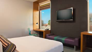 A hotel room with a large bed, a desk, a chair, a TV, and a window with a view.