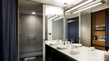 Un baño moderno con cabina de ducha de vidrio, tocador con dos lavabos y un espejo grande.