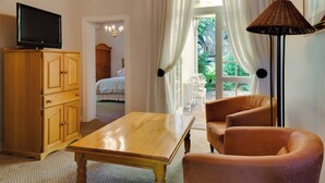 A hotel room with a wooden table, two leather chairs, a TV on a wooden cabinet, and a view of a garden through a window with white curtains. - Protea Hotel by Marriott Dorpshuis & Spa Stellenbosch (Stellenbosch)