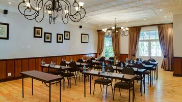 Un salón de conferencias con piso de madera, mesas, sillas y un candelabro.