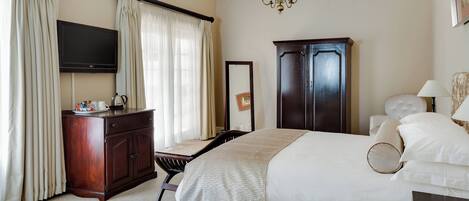 Habitación de hotel con cama, escritorio, armario, televisor y candelabro.