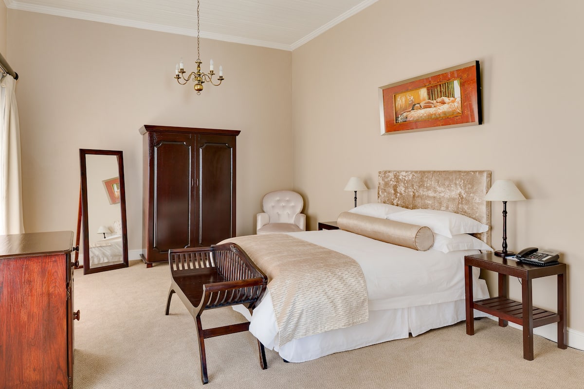 A bedroom with a large bed, bedside tables, a chair, a wardrobe, and a chandelier.